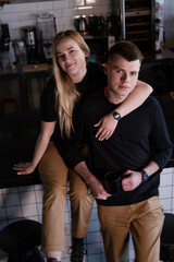 Fototapeta premium happy married couple in identical clothes family look - cafe owners or workers - in modern coffee shop. family business. loft cafe