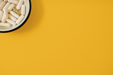 Vibrant colorful flat lay of medicine pill capsules filled with sugar candy sprinkles on yellow background. Creative concept of overdose medicine usage and addiction to food supplement.