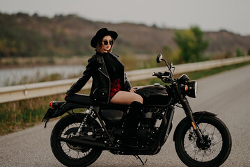 Fototapeta na wymiar Motorcyclist woman in mini skirt sitting on retro-styled motorcycle. Sexy female driver in jackboots on roadway. Trip, speed, freedom concept.