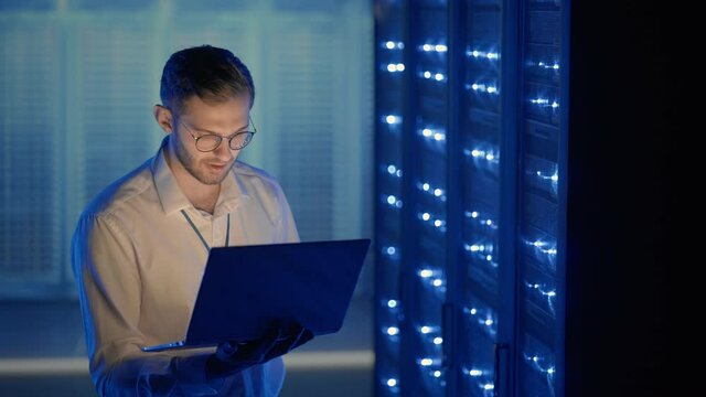 Male Server Engineer in Data Center. IT engineer inspecting a secure server cabinet using modern technology laptop coworking in data center.