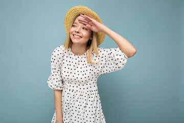 Photo of young positive happy smiling attractive blond lady with sincere emotions wearing summer dress and straw hat isolated over blue background with copy space