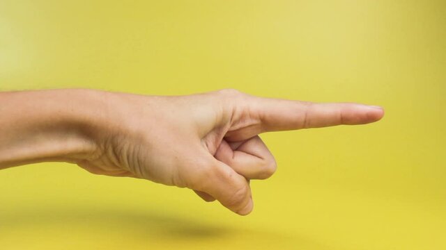 Woman hand with the index finger pointing to the side close-up on a yellow background. Advertising concept, announcements.