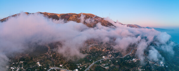 Aerial view of mountain massif over beach and Borsh city, evening pink light, clouds over mountains. Panoramic mountainscape and sea. Traveling around Albania, vacation in September in the Balkans. 