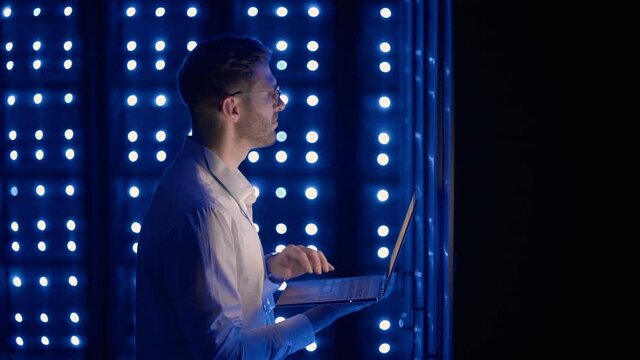 Male Server Engineer in Data Center. IT engineer inspecting a secure server cabinet using modern technology laptop coworking in data center.