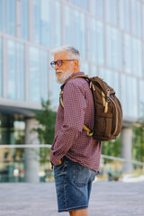 an adult gray-haired man with a beard goes to the office to work. a senior businessman in a shirt and with a laptop is making a career in a large company. a stylish European talks on the phone with