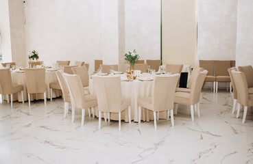 Wedding. Banquet. Chairs and a round table for guests, served with cutlery, flowers and utensils and covered with a tablecloth. Beige colors