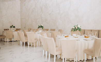 Wedding. Banquet. Chairs and a round table for guests, served with cutlery, flowers and utensils and covered with a tablecloth. Beige colors