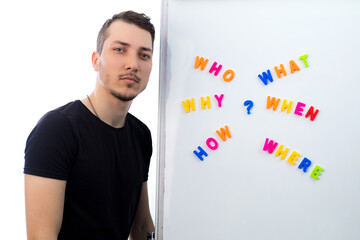 Young handsome man meditates thoughtfully while standing at the blackboard with questions on light...