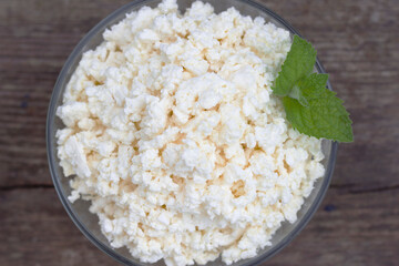 Glass bowl of farm curd with fresh green mint leaves. Cottage cheese on the old wooden table with top view. Natural food with calcium and protein for tasty breakfast.