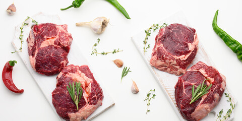 raw piece of beef ribeye with rosemary, thyme on a white table, top view