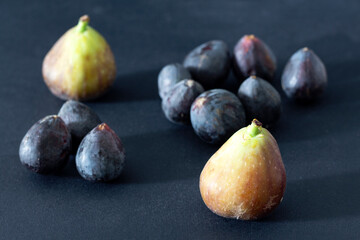 Large green and small black ripe figs on a black background.