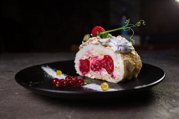 biscuit roll with berries on a stylish black plate close-up