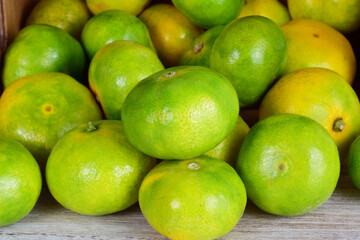 Close up, tangerine with green skin, more units behind in a group, next to a lying wooden box.