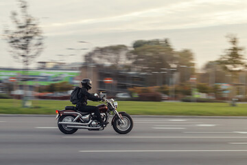 A motorcycle rides on the street at high speed in front of the rising sun. The motorcyclist dressed...