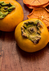 fresh whole ripe Japanese persimmons and dried fruit slices of persimmon on wood board autumn colors