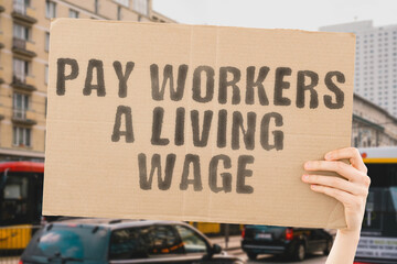 The phrase " Pay workers a living wage " on a banner in men's hand with blurred background. Money. Earnings. Payment. Financial crisis. Employment. Employees