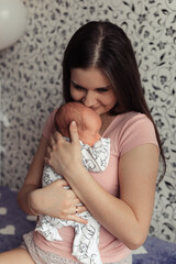 Mother holding tight newborn daughter on her arms. Young brunette female kissing head of her baby. Selective focus. Film grain