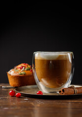 Cappuccino or cocoa with milk foam. In a glass goblet and a pumpkin muffin in the background. vertical, copy space, low key