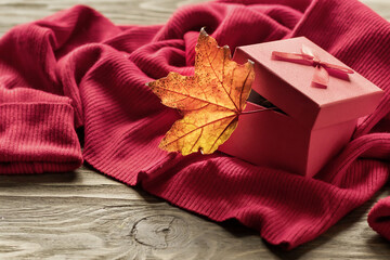 Maple autumn leaf in a gift box on the background of a warm sweater on a wooden table. Autumn sales and gifts. Copy space.