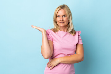 Middle age woman isolated on blue background holding copyspace imaginary on the palm to insert an ad