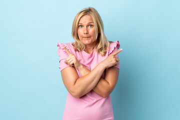 Middle age woman isolated on blue background pointing to the laterals having doubts