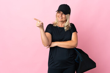 Middle age woman with sport bag isolated on pink background pointing finger to the side