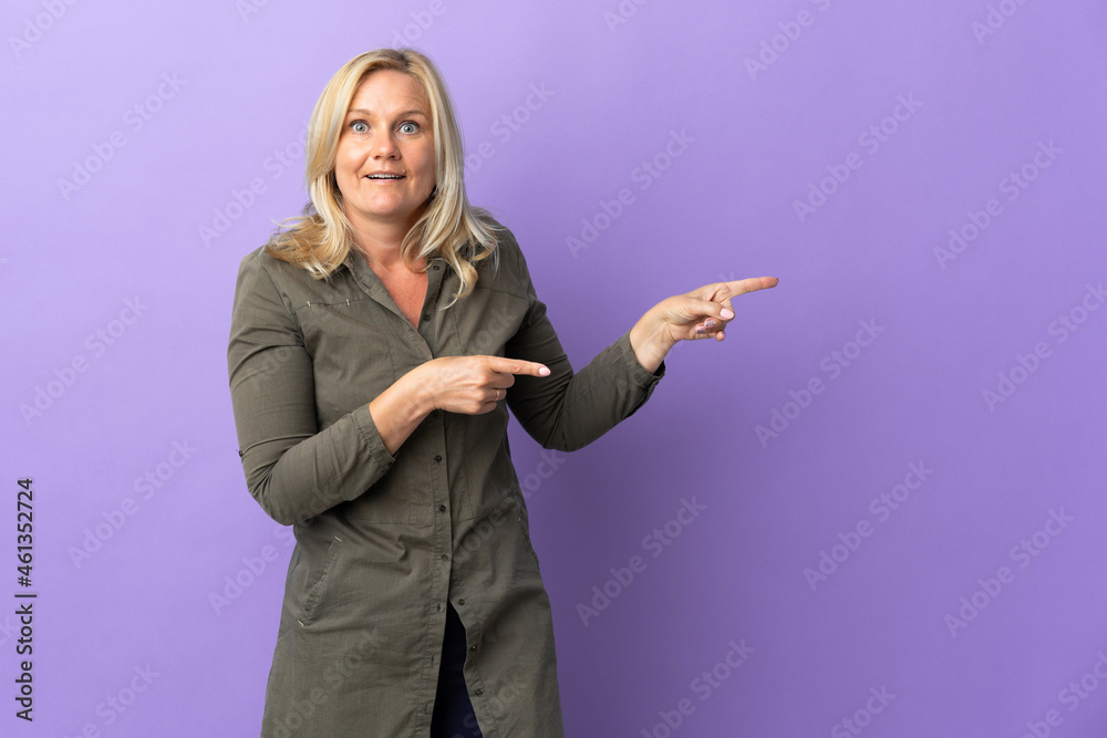 Wall mural Middle age Lithuanian woman isolated on purple background surprised and pointing side