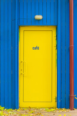 Bright yellow cafe door on colorful blue wall, fallen leaves
