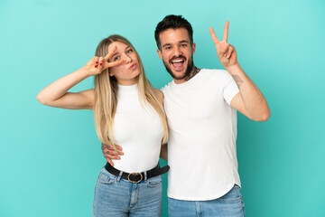 Young couple over isolated blue background smiling and showing victory sign