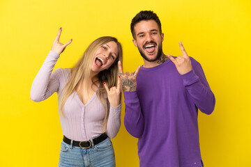 Young couple over isolated yellow background making rock gesture
