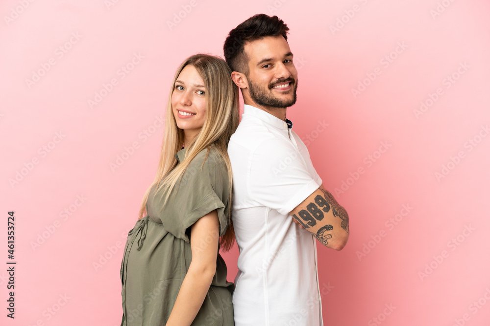 Poster Pregnant woman and man over isolated pink background keeping arms crossed