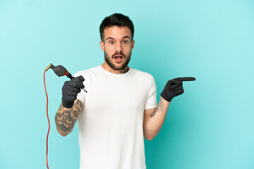 Tattoo artist man over isolated blue background surprised and pointing finger to the side
