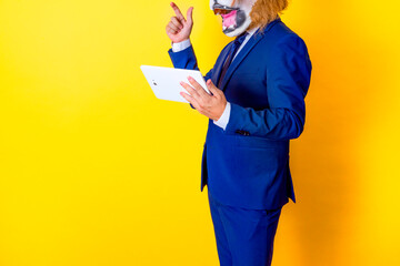 Unrecognizable businessman wearing lion mask and holding tablet in hand. Yellow background with...