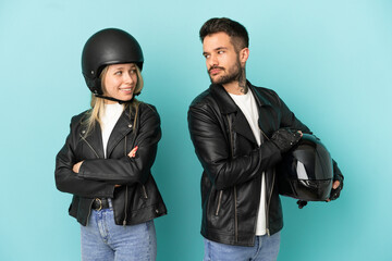 Couple with motorcycle helmet over isolated blue background looking over the shoulder with a smile