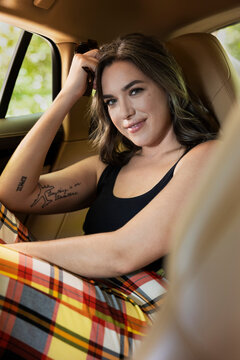 Portrait of caucasian casually dressed woman with tattoos sitting in backseat of luxury sedan 