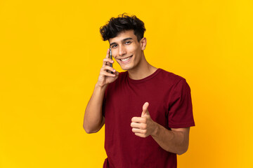 Young Argentinian man isolated on yellow background keeping a conversation with the mobile while...