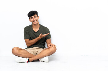 Young Argentinian man sitting on the floor presenting an idea while looking smiling towards