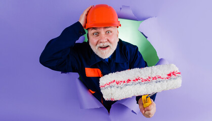 Painter man with painting roller through hole in paper. Worker in hard hat and uniform. Advertising.