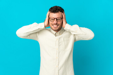 Young caucasian handsome man isolated on blue background frustrated and covering ears