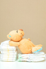 Stack of diapers with teddy bear toy lying on white table. set for children, baby shower party