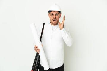 Young architect man with helmet and holding blueprints isolated on white background with surprise and shocked facial expression