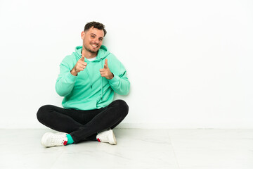 Obraz premium Young handsome caucasian man sitting on the floor pointing to the front and smiling