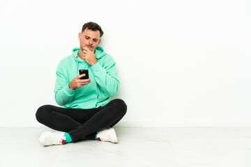 Young handsome caucasian man sitting on the floor thinking and sending a message