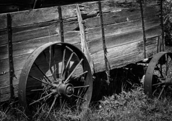 Fototapeta na wymiar Black and white image of an old wooden cart with rusted metal wheels. The wood is weathered and rotting. The viewer gets a good impression of what life and transportation was like many years ago.
