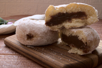 Fresh homemade sugar powdered donuts with chocolate cream filling on wood table