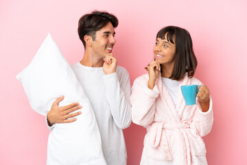 Young couple in pajamas isolated on pink background looking looking at each other