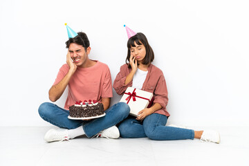 Young mixed race couple celebrating a birthday sitting on the floor isolated on white background unhappy and frustrated with something