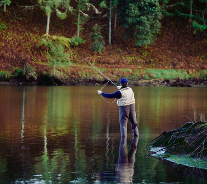 Back view of man wading in water and casting line fishing for trout in autumn