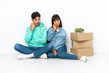 Fototapeta na wymiar Young couple making a move while picking up a box full of things sitting on the floor isolated on white background looking to the front