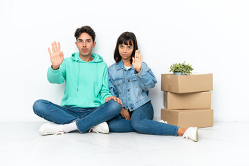 Young couple making a move while picking up a box full of things sitting on the floor isolated on white background making stop gesture denying a situation that thinks wrong